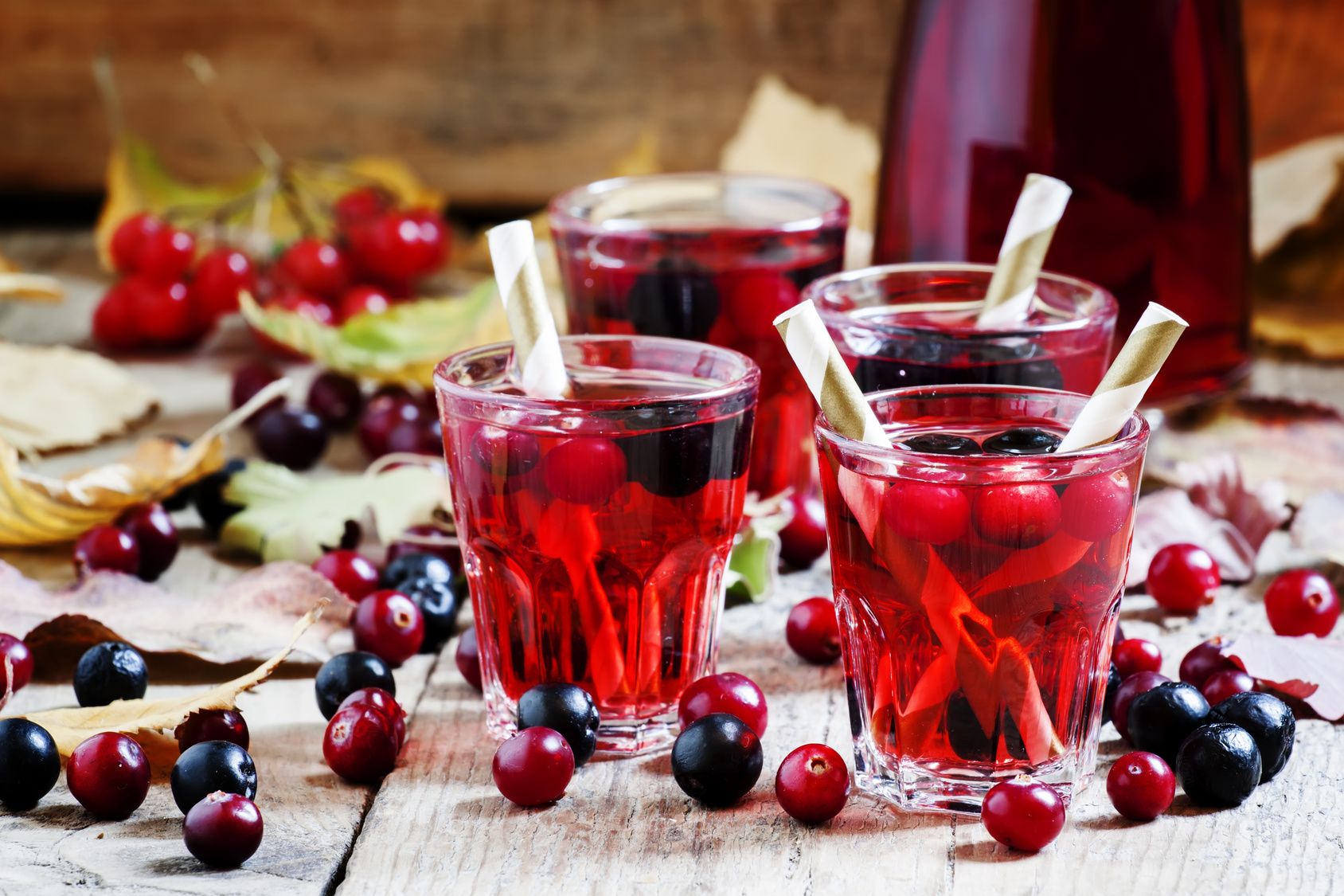 Eistee aus Lapacho Gläser mit einer klaren roten Flüssigkeit auf einem Tisch. Dort liegen einzelne Beeren