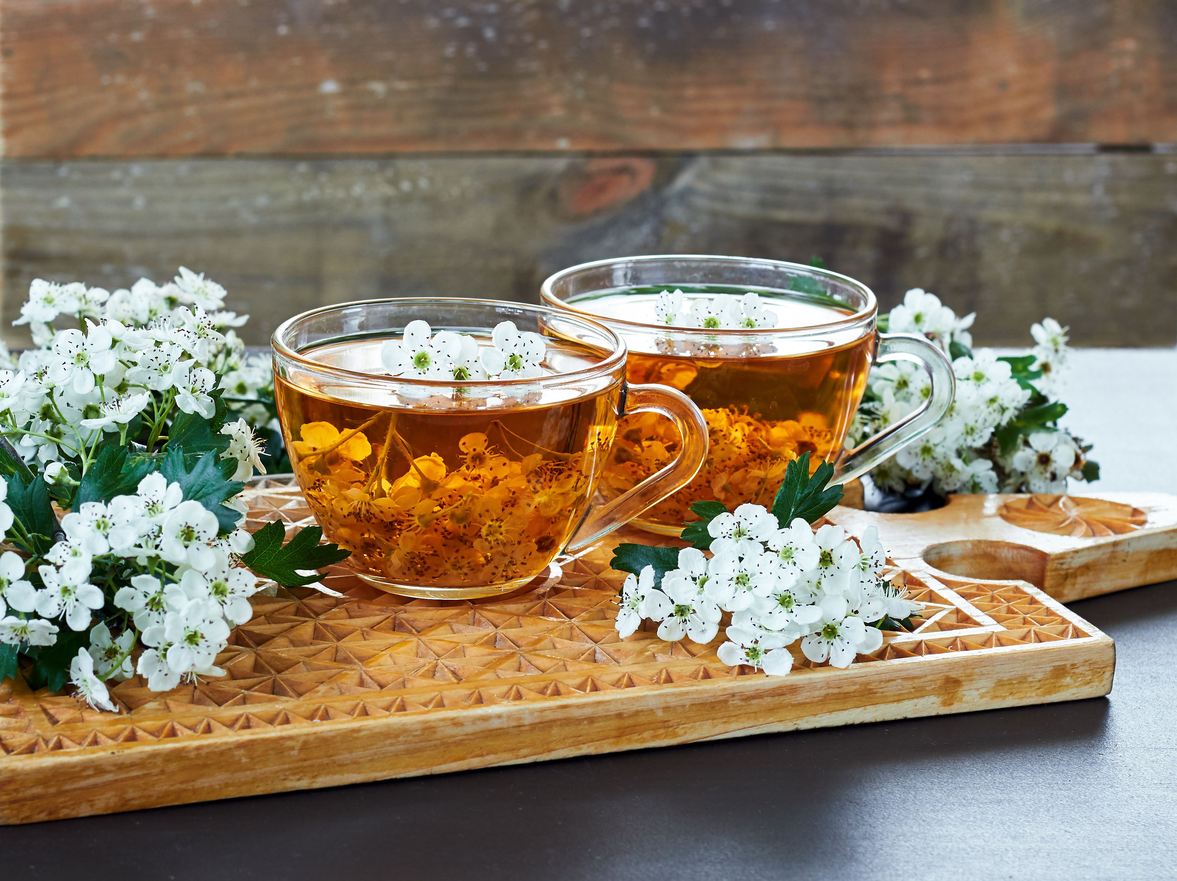 Zwei Teetassen aus Glas mit Weißdorn Tee, davor einige Weißdornblüte