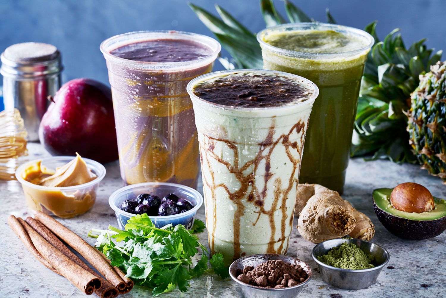 Drei leckere Smoothies auf einem Tisch umgeben von unterschiedlichen Zutaten Drei leckere Smoothies auf einem Tisch umgeben von unterschiedlichen Zutaten